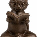 Bronze resin figurine of a cat with glasses, sitting cross-legged and reading an open book, on a light surface.