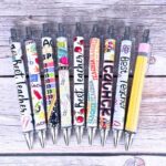 A close-up view of ten YJ PREMIUMS multicolor retractable ballpoint pens with various teaching-themed designs.