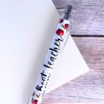 A close-up view of ten YJ PREMIUMS multicolor retractable ballpoint pens with various teaching-themed designs.